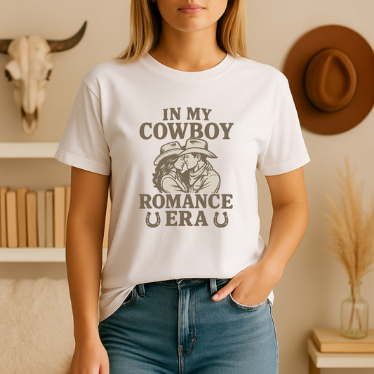 ChatGPT said:
A young woman stands in a softly lit reading nook wearing a white bookish t shirt printed with “In My Cowboy Romance Era” above a vintage-style illustration of a cowboy and cowgirl leaning in for a tender kiss framed by horseshoes; she pairs it with light-wash jeans and minimal jewelry, with neutral-toned bookshelves and pampas grass softly styling the background.